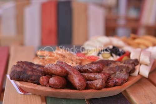 Fried sausages with herbs and grilled meat, all placed on a wooden tray.