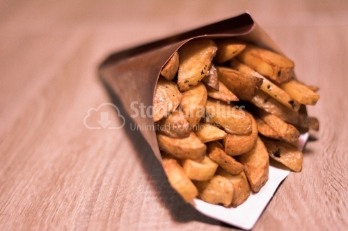 Potatoes wedges in paper cone on a wooden table