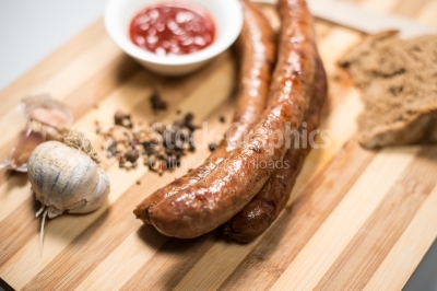 Sausage on a wooden plate with pepper, bread and garlic