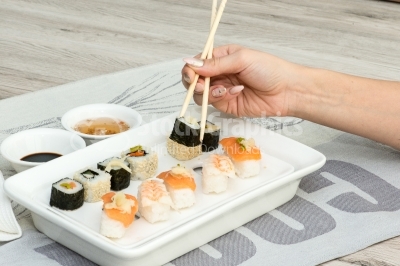 Sushi rolls aranged by a woman hand on a white plate