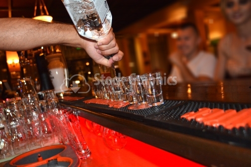 Bartender pours vodka into glasses