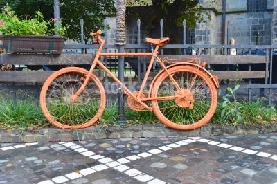 Decorative orange bicycle resting on a sidewalk