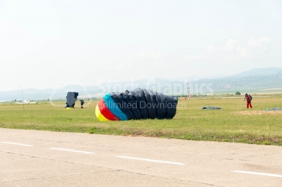 Landed skydivers with colorful parachutes on meadow