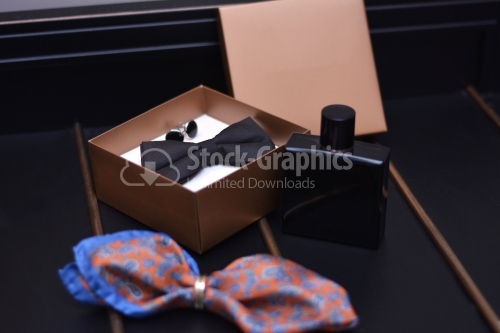 Set groom bow ties, cufflinks, and perfume on dark background.