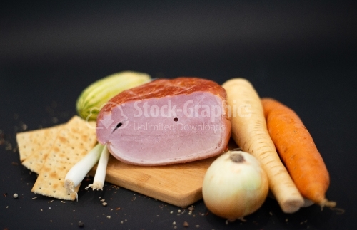 Smoked ham on a cutting board with lots of vegetables