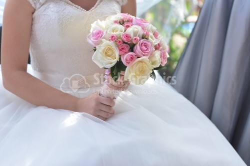The bride is sitting on the chair with the bouquet in her hand.