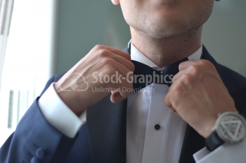 The groom places his bow tie.