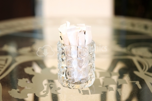 Thick glass cup filled with sugar sachets.
