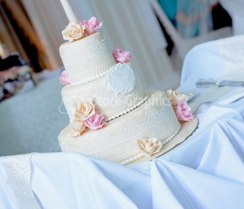 White wedding cake with lace and pink and beige roses on top
